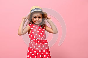 Cute Caucasian baby girl in pink summer dress and straw hat posing over pink wall background with copy space. Studio portrait of