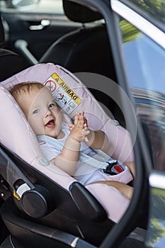 Cute caucasian baby girl ten months old smiling in child safety seat in car during road trip. Adorable infant sits in