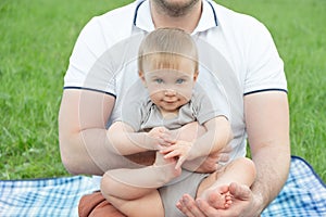 Cute caucasian blonde baby girl or boy looking at camera in hands of his unrecognizable father athletically built