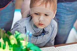 Cute caucasian blonde boy blows out the candles on the birthday cake.