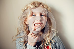 Cute Caucasian blonde girl showing her missing tooth in mouth. Proud child kid showing lost tooth and expecting a tooth fairy