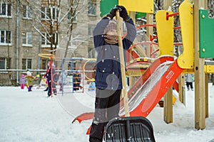 Cute caucasian boy with a big snow spade on playground in kindergarten