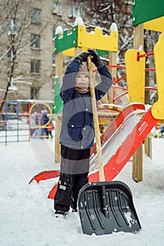 Cute caucasian boy with a big snow spade on playground in kindergarten