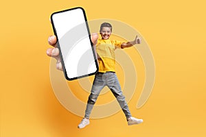 Cute caucasian boy jumping in the air, showing big phone