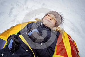 Cute caucasian boy laying on snow tubing and smiling. Winter activities on fresh air