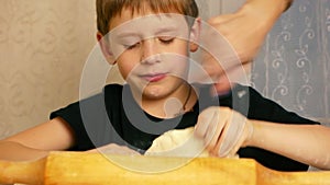 Cute caucasian boy prepares pizza dough in the kitchen, mom`s hand jokingly touches his nose. Fun time in the home kitchen. Kid le