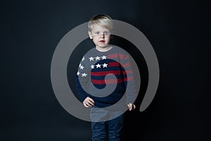 Cute caucasian boy in sweater with USA American flag on black background with copy space