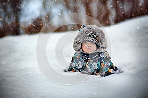 cute caucasian boy in warm winther jacker with fur hoody laying in snow in countryside on winter day