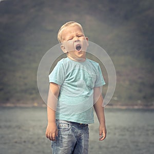 Cute caucasian boy yawns at seaside