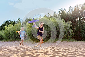 cute caucasian boys running along beach going to launch a toy plane.