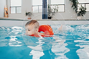 Cute Caucasian child boy in swimming pool with red float ring. Preschool boy training to swim in water indoors. Healthy active