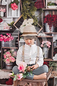 Cute Caucasian child sitting on a stool, surrounded by a bouquets of roses