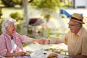 Cute caucasian elderly couple enjoy outdoor, having breakfast and coffee, holding hands