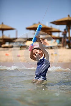 Cute caucasian four year old girl in swimsuit playing with a toy pump in the sea interior