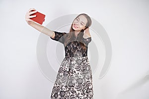 Cute caucasian friendly girl stands with a mobile phone in her hand and takes a happy emotional selfie on a white background in th