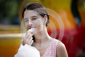 Cute caucasian girl in amusement park is eating pink candyfloss. Portrait of happy attractive young woman with cotton candy.