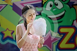 Cute caucasian girl in amusement park is eating pink candyfloss. Portrait of happy attractive young woman with cotton candy.