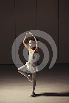 Cute caucasian little ballerina in white ballet costume and pointe shoes dancing in studio