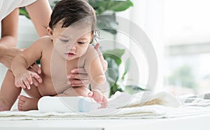 Cute Caucasian little naked toddler baby girl sitting on towel after bathing is playing talcum powder bottle while mother holding