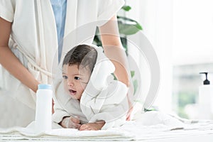 Cute Caucasian little toddler baby girl wear bathrobe after bathing is smiling and lying on towel while mother wipe her dry