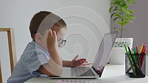 cute caucasian preschooler child glasses sitting at desk using laptop computer