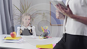 Cute caucasian schoolgirl jumping up at the table and making victory gesture. Unrecognisable female tutor standing at