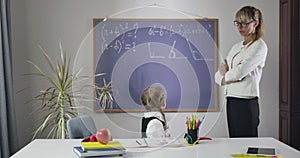 Cute Caucasian schoolgirl looking back at blackboard, turning back to camera and putting head on hands. Middle aged