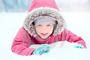 Cute Caucasian smiling excited girl child in pink jacket playing with snow. Kid lying on ground during cold winter snowy day at