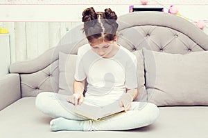 Cute caucasian teenage girl is sitting on the sofa with a book
