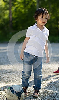 Cute caucasian toddler boy playing with soccer ball in the park at sunny day