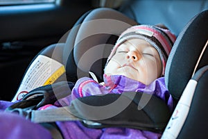 Cute Caucasian toddler boy sleeping in child safety seat in car during road trip