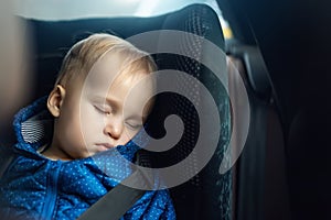 Cute caucasian toddler boy sleeping in child safety seat in car during road trip. Adorable baby dreaming asleep in comfortable