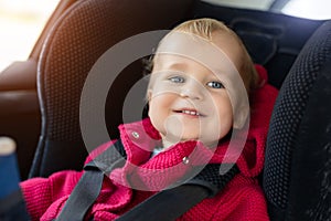 Cute caucasian toodler boy sitting in child safety seat in car during road trip. Adorable baby smiling and enjoying trip in