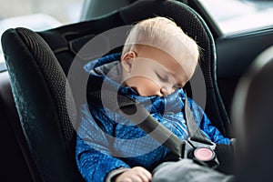 Cute caucasian toodler boy sleeping in child safety seat in car during road trip. Adorable baby dreaming asleep in comfortable