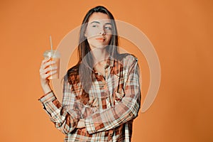 Cute caucasian young brunette girl holding orange juice on orange background