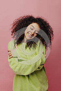 Cute caucasian young woman hugging herself with her eyes closed, feeling warm on pink background.