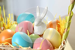 Cute ceramic Easter bunny and dyed eggs in wicker basket on table