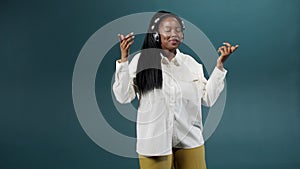 A cute charming african woman in a white blouse with earpieces is dancing on color background photo