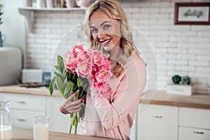 Cute charming girl with a bouquet of tulip flowers presented by her daughter in the kitchen