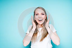 A cute charming girl with long hair rejoices and smiles broadly.  on blue background photo