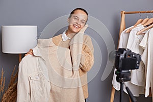 Cute charming satisfied smiling woman wearing beige jumper, showing warm soft sweater, creating content for her vlog, recording