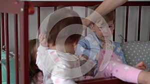 Cute cheerful 3 little kids girl and boy siblings preschool children in grey baby crib after waking up from sleep in