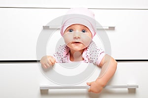 Cute cheerful baby, sitting in a drawer chest