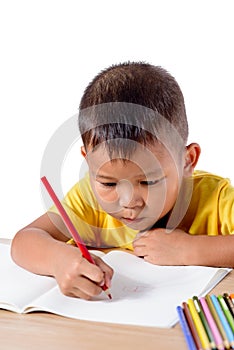 Cute cheerful child drawing using color pencil while sitting at table isolated on white background