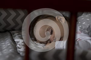 Cute cheerful little chubby baby girl sleeping sweetly in grey baby crib during lunch rest time in white and pink