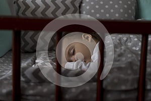 Cute cheerful little chubby baby girl sleeping sweetly in grey baby crib during lunch rest time in white and pink