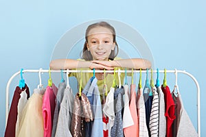 Cute cheerful little girl chooses clothes with floor hangers.