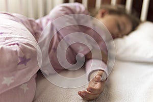 Cute cheerful little 3-4 years preschool baby girl kid sleeping sweetly in white crib during lunch rest time in pink