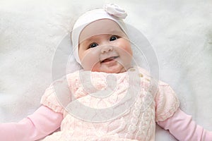 Cute cheerful newborn dressed in pink sweater on white fur blanket. Adorable infant baby with headband.