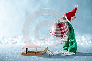 Cute Cheerful Santas Helper Elf Loading Christmas Bauble Onto Santas Sleigh. North Pole Christmas Scene. Elf at work.